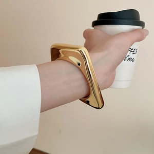 Close-up of a glossy gold irregular geometric bracelet worn in a minimalist lifestyle setting