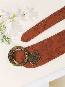 Detailed close-up of brown leather belt with floral embossing and bronze rivet studs