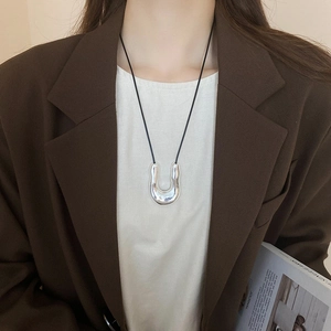 Detail of silver U-shaped metal pendant on minimalist black cord necklace against brown suit