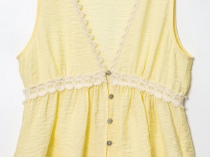 Detail of yellow sleeveless top featuring white lace trim and vertical pleated texture