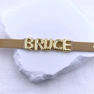 Detailed view of a gold mesh watch strap featuring sliding DIY metal letter charms spelling BRUCE