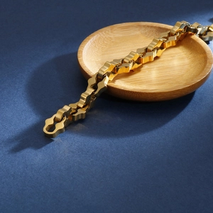 Détail macro d'un bracelet à chaîne géométrique plaqué or 18 carats sur un plateau en bois