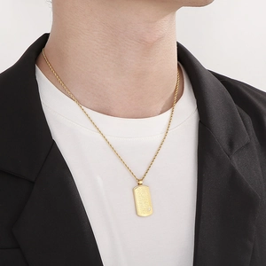 Gros plan d'un collier plaque rectangulaire dorée avec gravure et cristal sur un mannequin