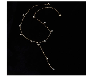 Close-up of golden Y-shaped necklace with white pearls and beads on black background