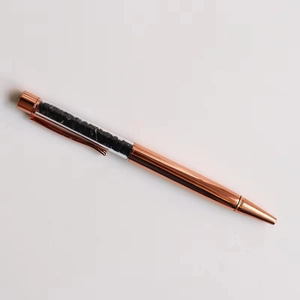 Detail of rose gold ballpoint pen with transparent barrel filled with black crystals