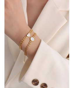 Macro detail of leaf-textured 18K gold chain with heart and round white shell pendants
