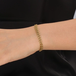 Close-up of a golden leaf chain bracelet worn on the wrist against dark silk fabric