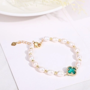 Detail of a pearl bracelet with gold beads and a green four-leaf clover charm decoration