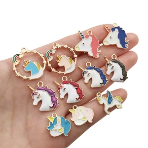 Detailed view of eleven colorful enamel unicorn charms for DIY jewelry on a palm