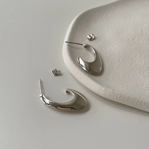 Macro view of polished silver U-shaped hoop earrings and butterfly backings on a white tray