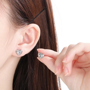 Détail des boucles d'oreilles cœur en argent avec pierre précieuse sur l'oreille du mannequin