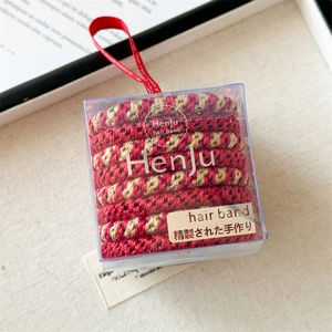 Detail of red and gold elastic hair bands in a clear gift box with a red ribbon strap