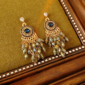 Detailed macro view of bohemian gold earrings with blue gemstone and grey-green crystal tassels