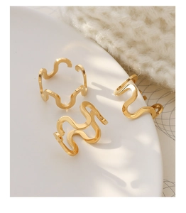 Close-up of three gold wavy U-shaped titanium steel rings on a minimalist white plate