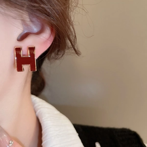 Macro close-up of H-shaped gold earrings with deep red enamel on a female model