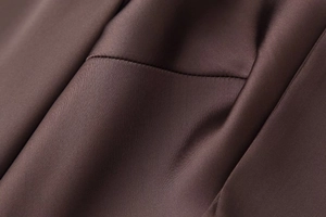 Detail of dark brown satin fabric showing smooth texture and precision stitching