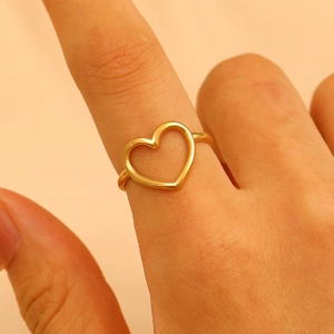 Close-up of minimalist gold hollow heart ring on finger with soft warm lighting