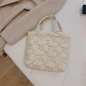 Detailed macro view of quilted rabbit embroidery and Simple Wish tag on cream tote bag