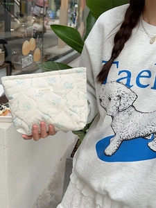 Quilted floral makeup bag in cream cotton fabric held by a model in a casual setting
