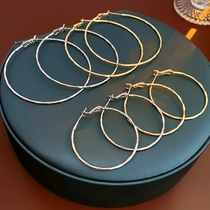 Close-up of wavy texture round hoop earrings in gold, silver, and rose gold on leather