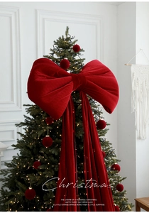 Close-up of a giant burgundy velvet bow as a Christmas tree topper in a cozy setting