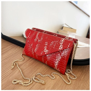 Detail of red crocodile textured envelope bag with white pattern and gold chain strap