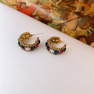 Detail view of gold C-shaped earrings with colorful inlaid crystals in baroque style