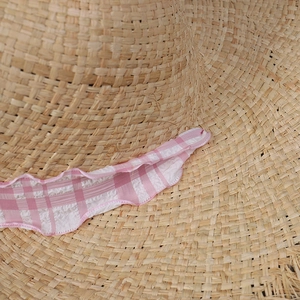 Detailed macro view of woven raffia sun hat with pink gingham ribbon trim texture