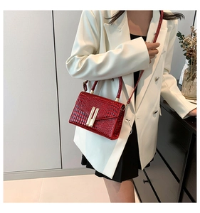 Detail of red crocodile texture handbag with gold metal hardware on model in white suit