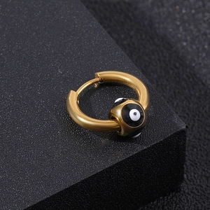 Golden stainless steel hoop earring with evil eye bead charm on textured black surface
