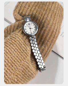 Detail of silver honeycomb strap watch paired with a brown knitted sweater cuff