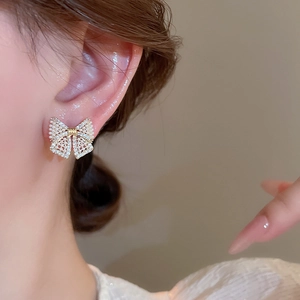Detailed view of gold bow earring with faux pearls and rhinestones on model