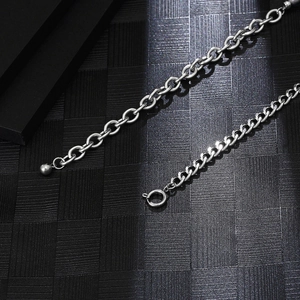 Macro detail of silver titanium necklace showing ball end and lobster clasp on black texture