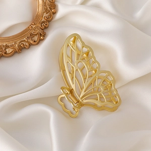 Detail of a matte gold butterfly hair claw clip with cutout wings on white silk fabric