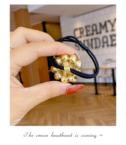 Detailed view of golden textured spherical bead charm on elastic black hair tie