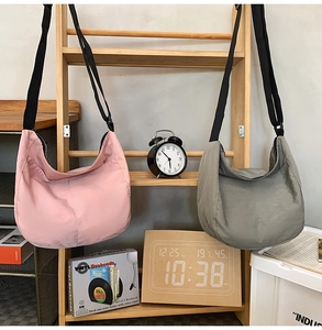 Pink and grey minimalist nylon crossbody bags hanging on a wooden rack with decor