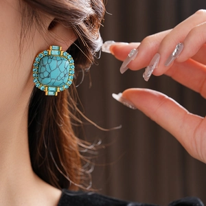 Macro shot of vintage gold earrings with turquoise and blue rhinestones on model