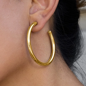 Elegant large golden stainless steel hoop earrings worn by a model in a side-profile view