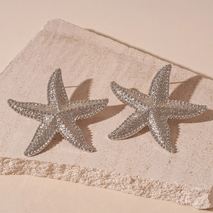 Close-up of silver starfish earrings with realistic textured surface on beige stone