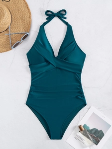Flat lay of dark green halter one-piece swimsuit with beach accessories on marble