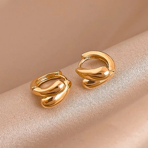 Detailed shot of polished gold twisted hoop earrings on soft champagne satin background