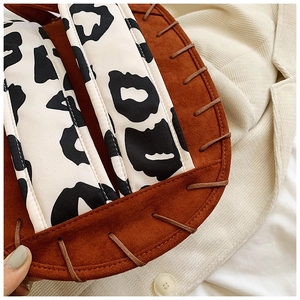 Close-up of brown suede saddle bag with cow print flap and woven leather trim details
