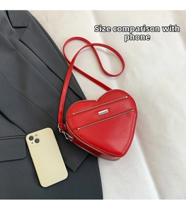 Red heart-shaped shoulder bag detail with zippers and size comparison to a phone