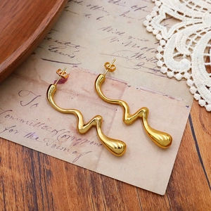 Détail macro des boucles d'oreilles vagues dorées avec texture de métal liquide sur papier