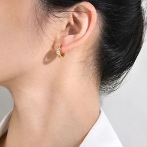 Close-up of gold hoop earrings with three vertical round zircons on a female model