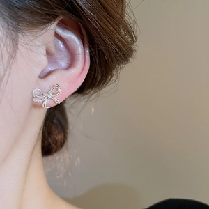 Close-up of polished silver bow stud earrings worn on ear with high precision detail