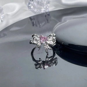 Close-up of silver bow ring featuring a pink heart-shaped gemstone on silk background