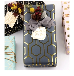 Dettaglio di carta regalo con motivi geometrici dorati, nastri di velluto e pigne decorative