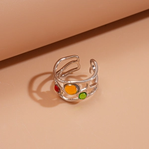 Gros plan d'une bague argentée avec des pierres rouges, jaunes et vertes sur fond rose