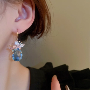 Detail of blue teardrop crystal earring with pink butterfly accent on a golden hook